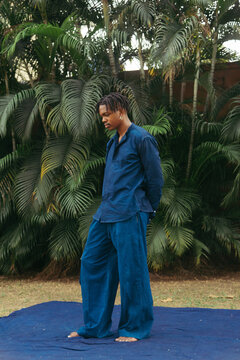A young black man dressed in blue standing outdoors amongst nature 