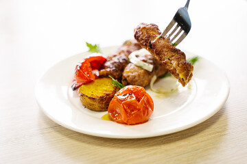 BBQ kebab with grilled vegetables, grilled meat, tomato, sweet pepper and onion on a plate, a piece of cutlet on a fork