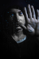 Portrait of a young hooded man holding his hand on a glass covered in water drops - focus on his face