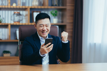 Young handsome happy asian businessman man rejoices, got good news, uses phone. Concluded an...