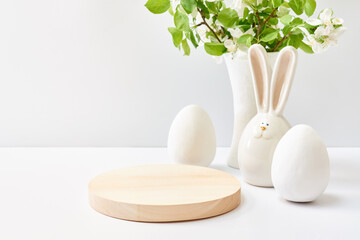 Empty round wooden podium for product presentation. Spring flowers in a vase, easter eggs on a light background. Mock up for displaying works