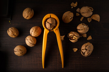 Nuts. Walnut kernels and whole walnuts. Walnuts organic in a black bowl with yelow metal nutcraker on a dark wood background. Top view. Walnut healthy food