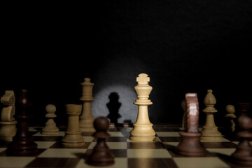 Chess king under spotlight. Studio shot of chess pieces on a chessboard illuminated by a stage light. Low-key.