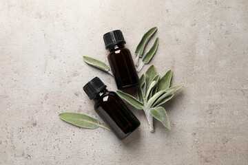 Bottles of essential sage oil, twigs and leaves on light grey table, flat lay