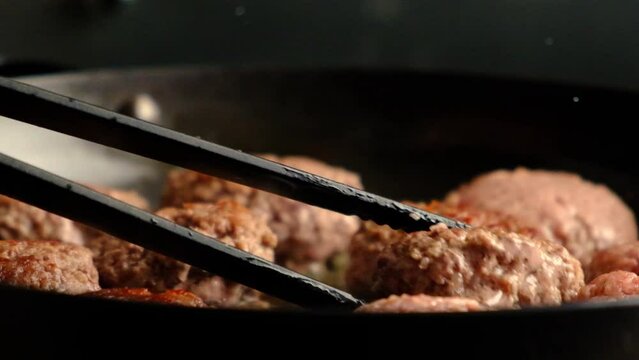 Chef grilling fresh meat cutlets for burgers - close up, slow motion. street food concept. Flipping meatballs in a black frying pan. 