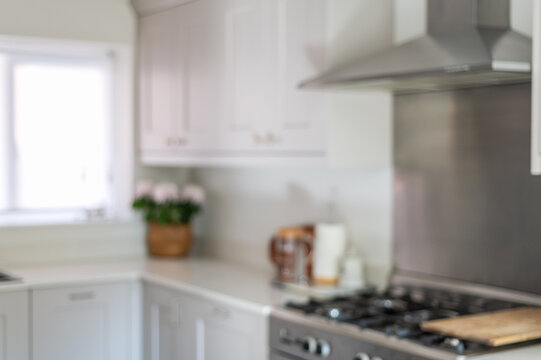 Blurred photo of modern new kitchen with light grey furniture and quartz worktop, light interior trendy units. Granite sink under big window