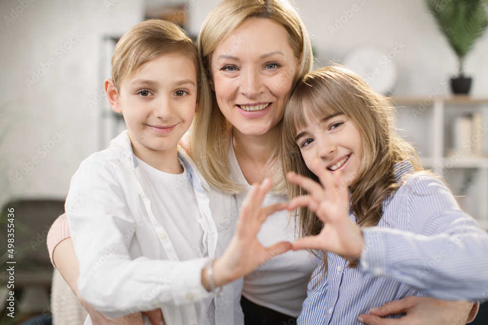 Wall mural Cute little daughter with son and mother join hands in shape of heart as concept of mom and kids love care support, smiling mum and her kids looking at camera posing together for headshot portrait