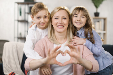 Portrait of little happy girl and boy and mother join hands forming heart shape as concept of giving love, child mum connection unity, cute kids and mom bonding looking at camera, child care adoption