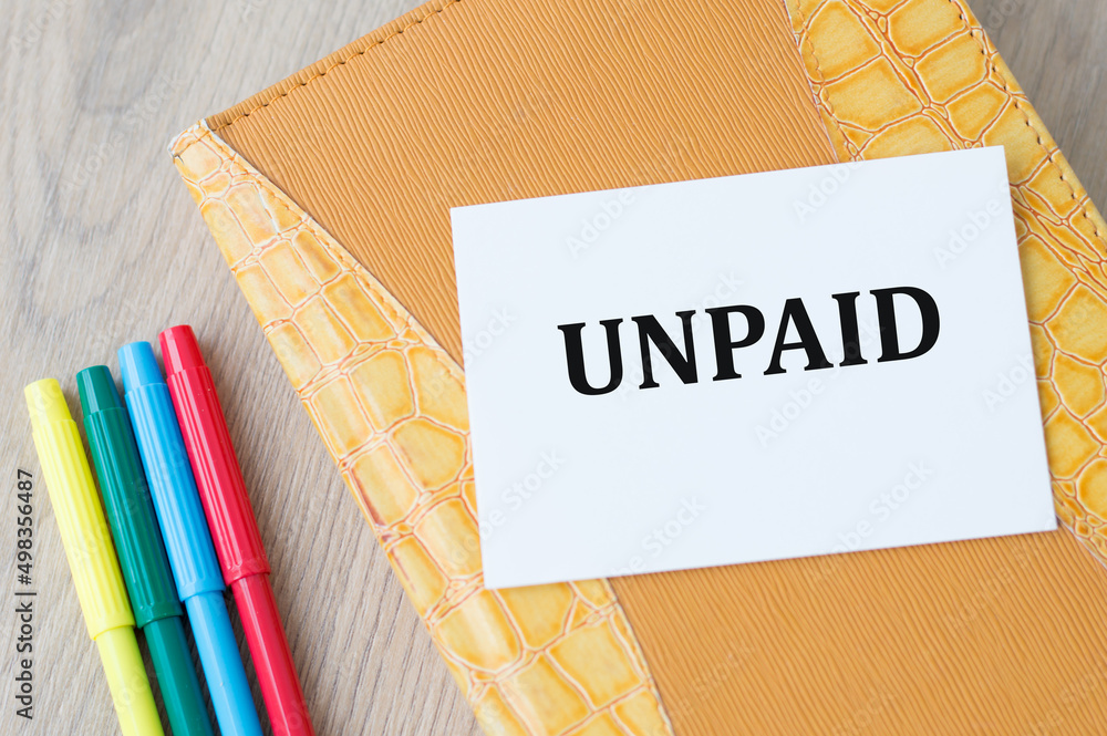 Poster unpaid inscription on the card on the background of a yellow notebook on the table with a rage of co