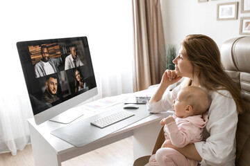 Working young mother in maternity leave work remotely or study at home on computer while infant daughter hold papers and looking at screen. Modern day mother of little child sit at desk use gadgets