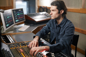 Portrait of male music producer using digital audio workstation while working with artists in...