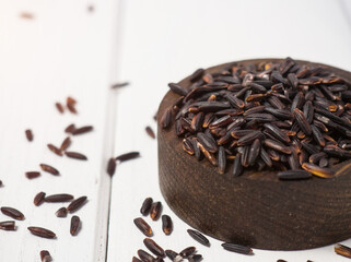 pile of black rice in a wooden bowl on a wooden table close-up