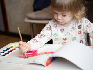 A 2-year-old girl sits at a table and learns to draw with multi-colored watercolors. Children's...