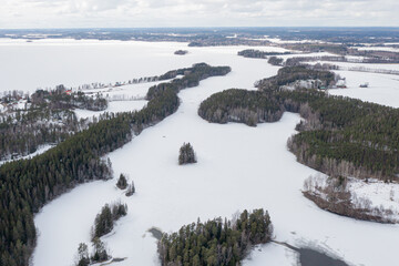 Obraz premium Landscape over a forest and a lake covered with ice and snow. Drone photo. Scandinavia. Finland.