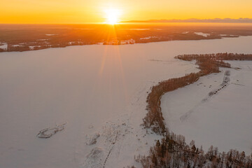 Sunrise over forest and ice-covered lake.Early sunrise in winter. Drone photo. Scandinavia. Finland.