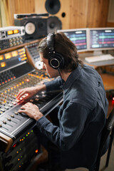 Side view portrait of man wearing headphones at audio workstation in recording studio, music...