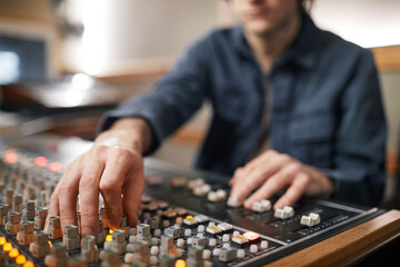 Close up of male hands operating buttons and toggles at audio workstation in professional recording...