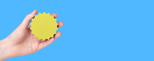 Yellow gear in hand over blue background. Banner with copy space for text. Artificial sun over heaven sky.