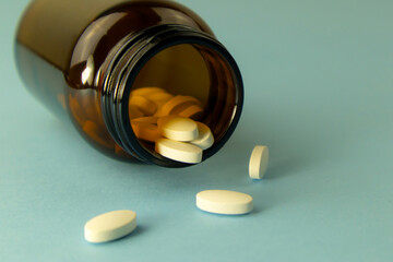 White pills falling out of glass drug bottle. Vitamins or medicine concept.
