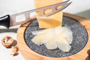 Close-up of parmesan slices, a piece of cheese and a knife on a wooden board - obrazy, fototapety, plakaty