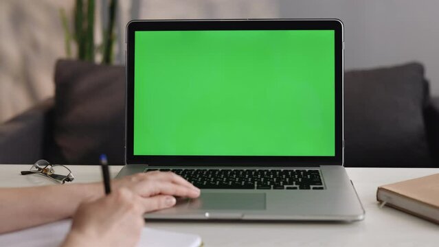 Young student girl looking at green screen laptop computer in living room watching education video content online. Unrecognizable business woman or female freelancer working from home office