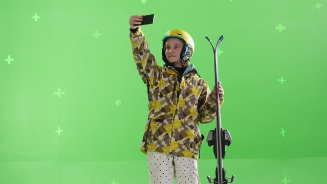 A young girl snowboarder taking a selfie against a green screen background in the studio. Active lifestyle in the mountains. Chroma key, tracking points