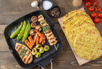 Grilled chicken steakand souvlaki in different variations with avocado, carrot, mushroom and brussels sprout on a teflon pan. Flat lay