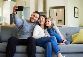 Well have these memories forever. Shot of a young family taking a selfie on the couch at home.