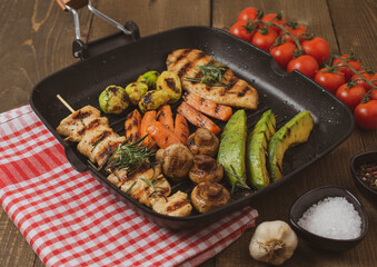 Grilled chicken steak in different variations with avocado, carrot, mushroom and brussels sprout on a teflon pan.
