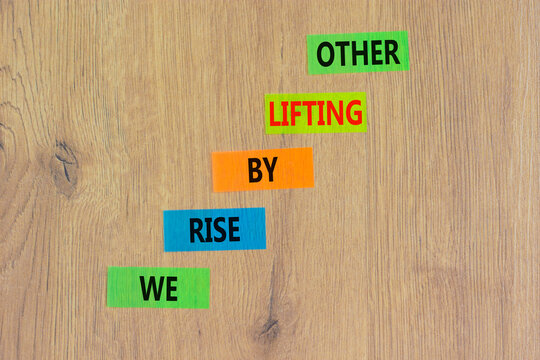 We rise by lifting other symbol. Concept words We rise by lifting other on colored paper. Beautiful wooden table wooden background. Business we rise by lifting other concept. Copy space.