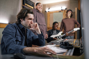 Side view portrait of music band composing new album in professional recording studio, focus on male producer in foreground