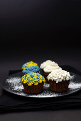 Chocolate cupcakes decorated with blue and yellow cream on a black background in support of Ukraine