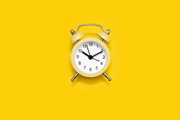 Yellow old-fashioned alarm clock with a dial on a yellow background. The concept of time and responsibility. Vintage look of the alarm clock