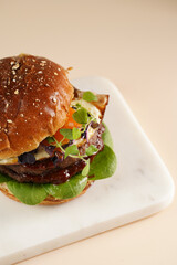 Hamburger with double angus beef patty, tomatoes, spinach, fried egg and barbeque sauce on marble board, pastel background