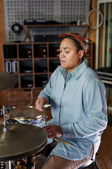 Vertical portrait of Latin American young woman playing drums in recording studio and making music