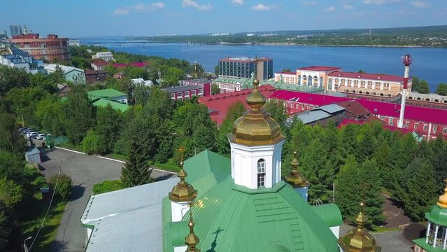 Aerial view of a summer city district with a church and houses. Clip. Beautiful green city located by the long river.