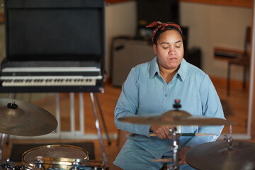 Portrait of focused female drummer playing music in professional recording studio, copy space