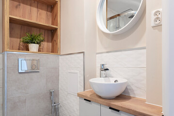 Fototapeta na wymiar Modern bathroom with white tiles, stylish bathroom sink with faucet, round mirror on the wall and wooden counter top. Luxury and new design in small bathroom at home.