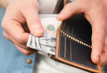 a man's hand takes out one hundred dollar bills from a purse