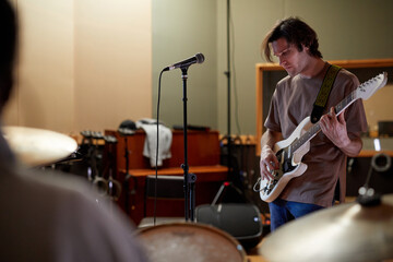 Portrait of young man playing electric guitar in recording studio in dim cinematic light, copy space