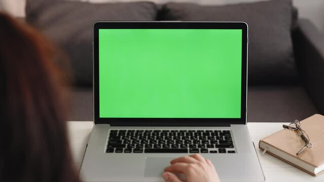 Over the shoulder shot of caucasian woman looking at green screen chroma key. Office person using laptop computer with laptop green mockup screen.
