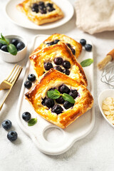 Mini puff pie with cheese cream, almonds, and blueberries in a plate on the kitchen table. Delicious layered square with berries, dorblue or ricotta, nuts on a culinary background	