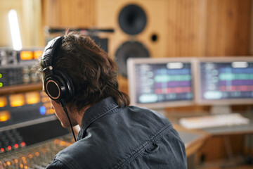 Male musician wearing headphones at audio workstation in professional recording studio, copy space