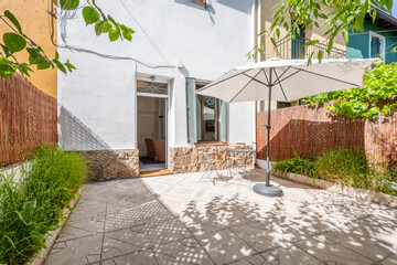 Fototapeta na wymiar Terrace of a single-family home with tiled floor, folding metal table and chairs under a parasol and plants in pots