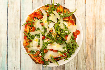 Top view image of pizza with a lot of arugula, parmesan flakes, tomato sauce and cherry tomatoes with olive oil