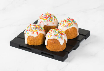 Holiday dessert. Easter small cakes with lemon sugar glaze, decorated with multicolored confectionery sprinkles,  on a wooden serving stand. White background