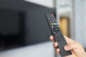Black remote control in hand in front of TV