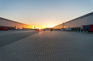 Logistics area with halls and trucks at sunset. Transport and storage of goods.