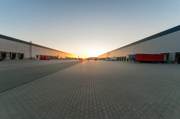 Logistics area with halls and trucks at sunset. Transport and storage of goods.
