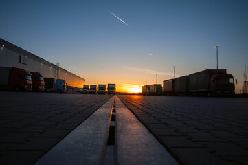 Fototapeta na wymiar Logistics area with halls and trucks at sunset. Transport and storage of goods.